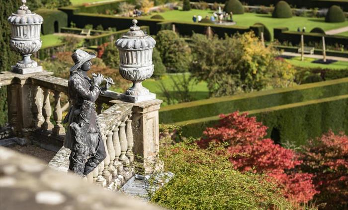 A lead statue on a stone terrace looking out onto green gardens with a long box hedge